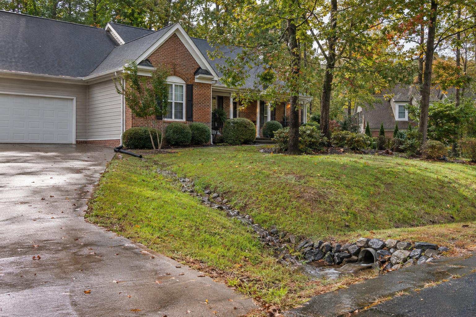 Illustrative photo: Sloping lawn, downspout extension, and roadside drainage swale beside a Piedmont North Carolina home after rain.